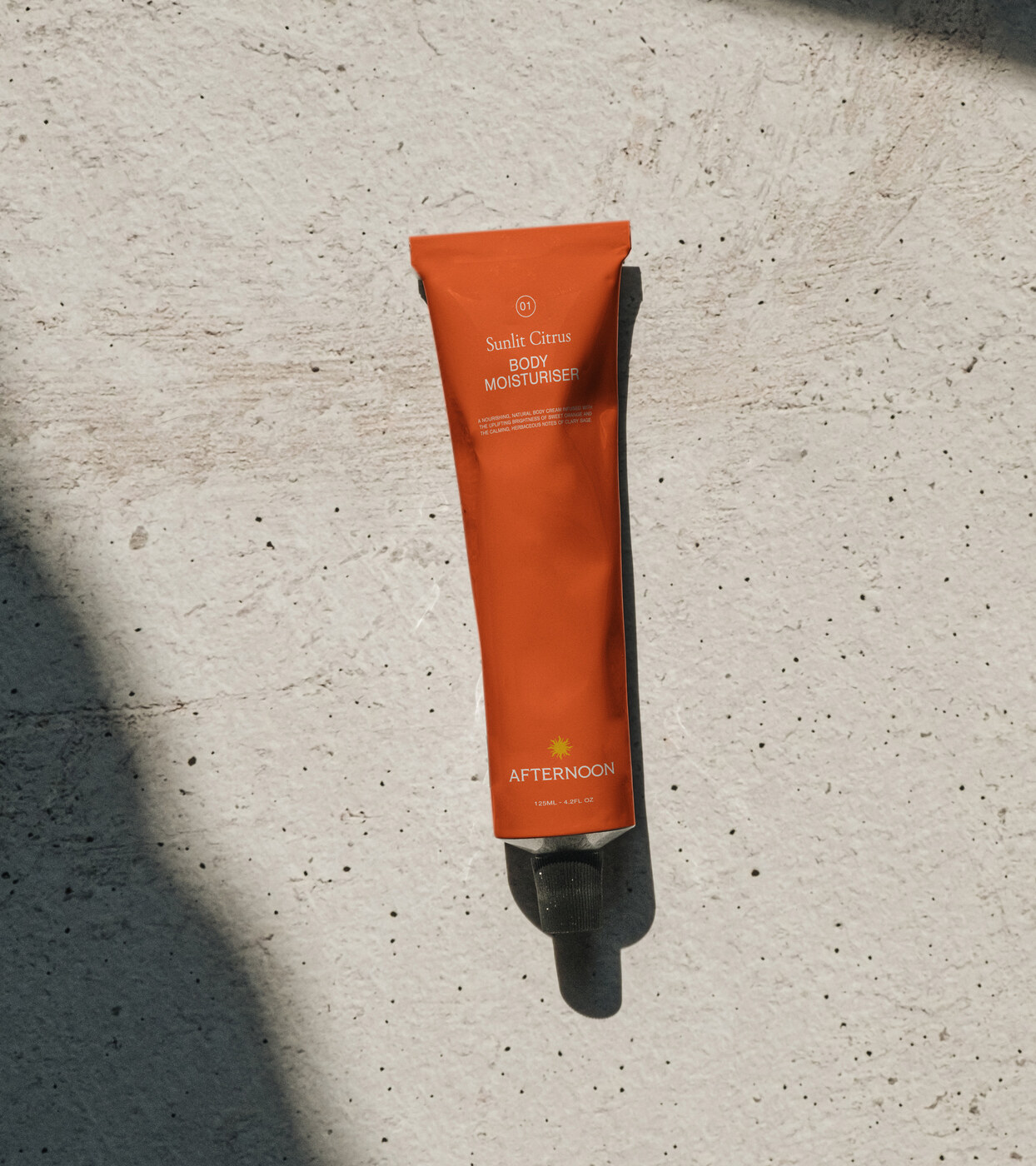 Sunlit Citrus body moisturiser tube on a sunlit stone surface